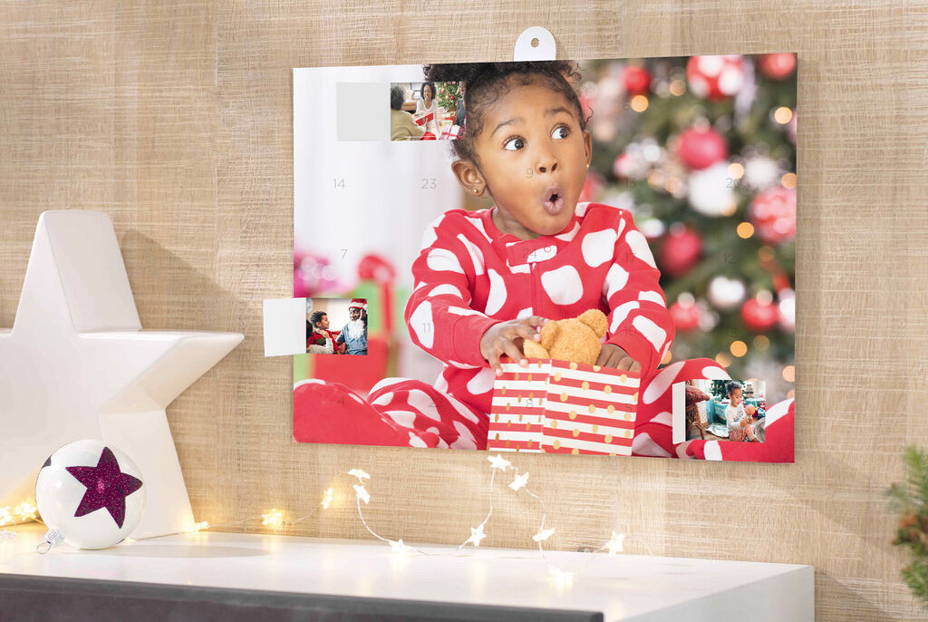 A child in a red pajamas with white dots holds a small gift bag. Christmas lights and decorations are in the background.
