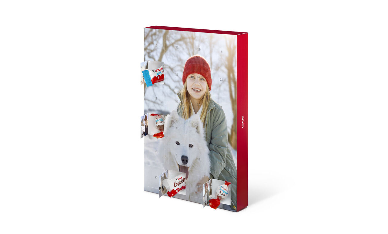 A young woman with a white dog in hand. She stands in a snowy landscape wearing a red hat. Blurred trees in the background.