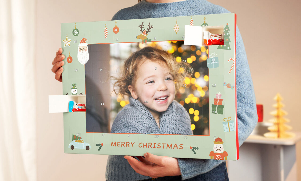 A person holds a cheerful frame with Christmas motifs and the text 'Merry Christmas'. Christmas tree lights are in the background.
